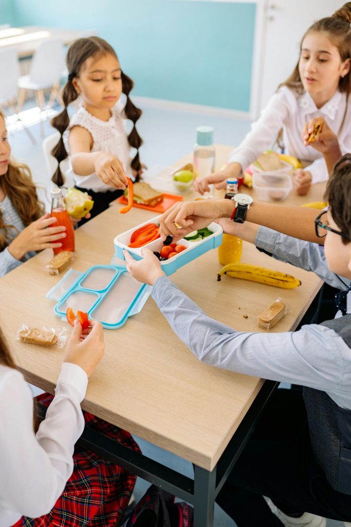 Group of children sharing healthy snacks at a school table indoors.