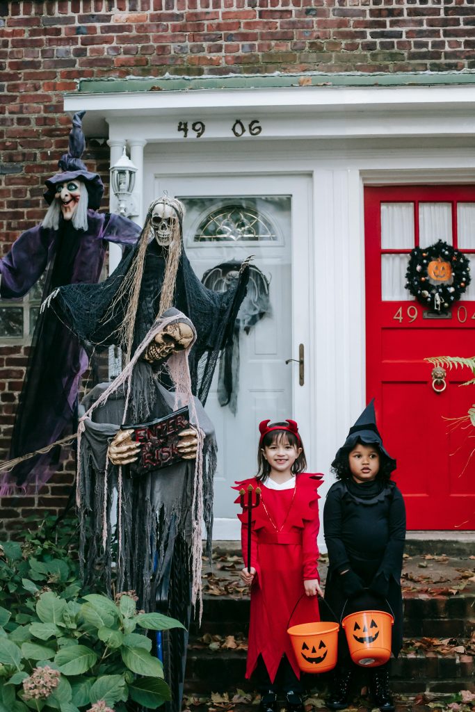 Cute children in devil and witch costumes trick-or-treating on Halloween.
